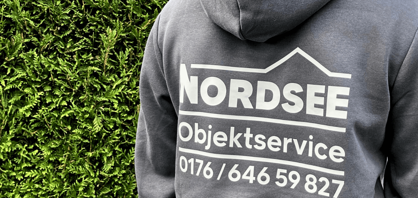 Mitarbeiter von Nordsee Objektservice mit Logo auf der Arbeitskleidung vor einer gepflegten Hecke in Jever.